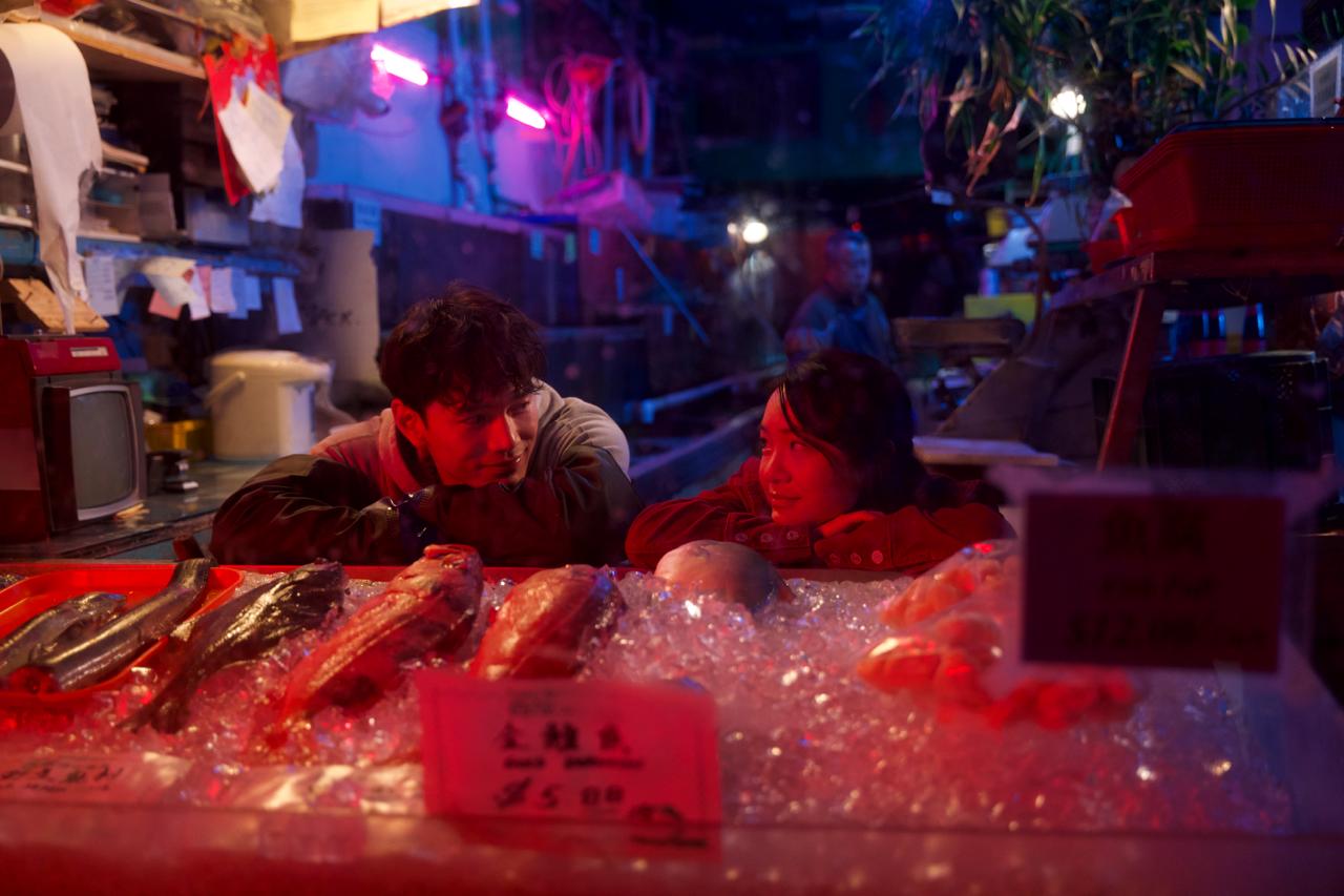 Nathan and Jenn lean on a neon-lit fish-market counter